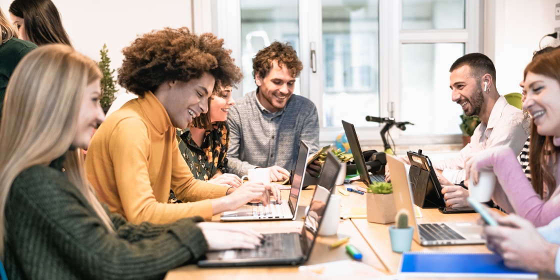Group of boot camp students sit around a table with their computers